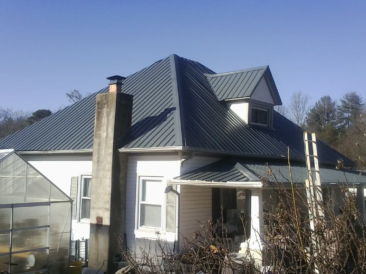 Dark blue standing seam metal roof on a white farmhouse with dormer — Slate & Tile Roof Repair by Roofing Brothers in Sanderson