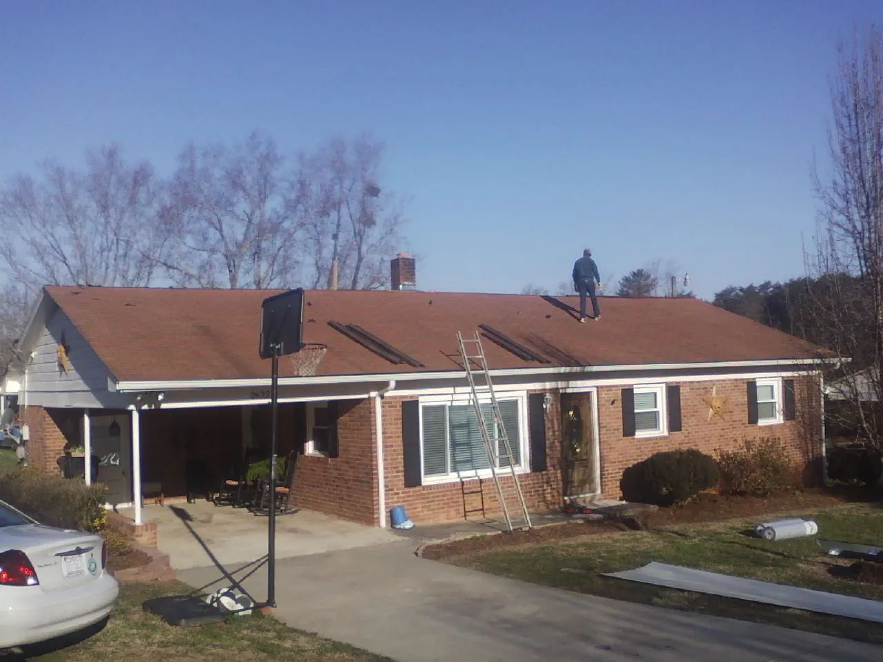 Roofer stripping a shingle roof on a brick ranch before metal panels in Sanderson