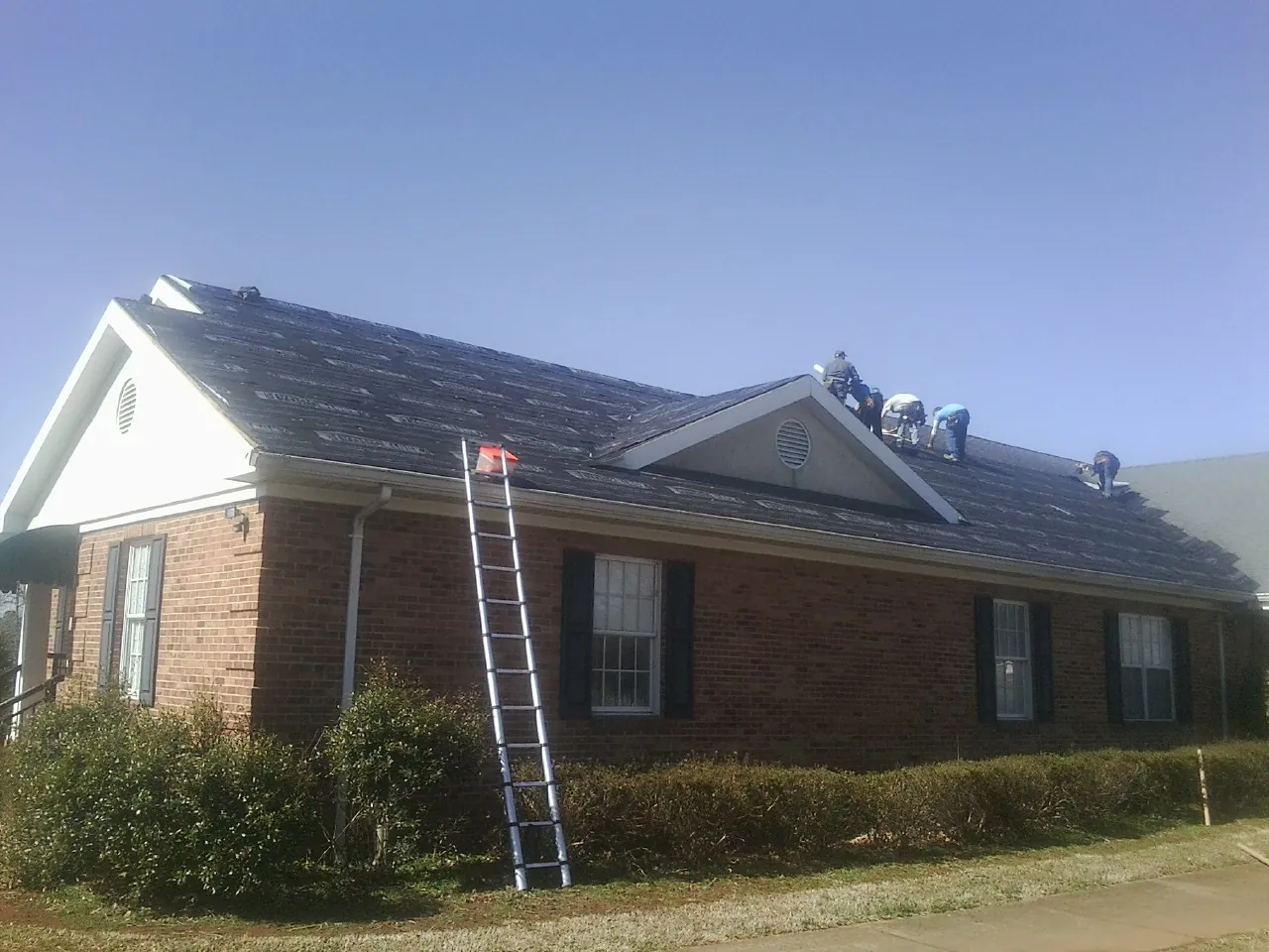 Crew tearing shingles off a brick ranch roof with a ladder set — Emergency Roof Repair work by our crew in Sanderson