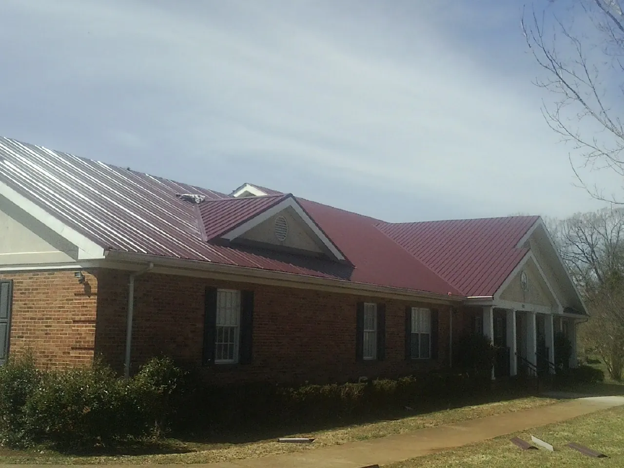 Red metal roof with gabled entries on a long brick building, from a Hail Damage Roof Repair job in Sanderson