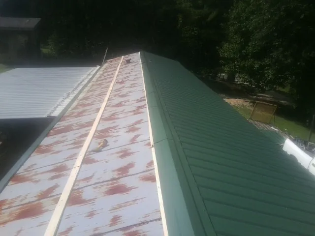 Old rusted panels beside newly installed green metal roofing — Wind Damage Roof Repair by Roofing Brothers in Sanderson