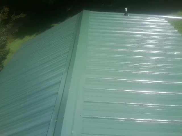 New green metal panels meeting at the ridge of a roof — Flat Roof Repair work by our crew in Sanderson