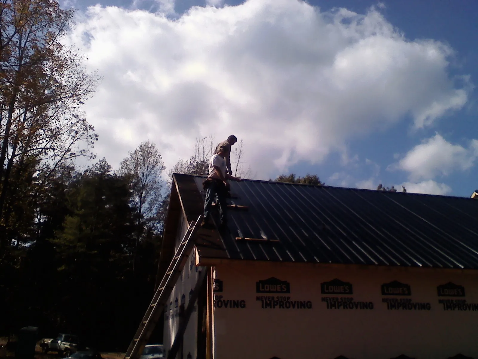 Roofer fastening dark metal panels high against a cloudy sky, from a Roof Inspection job in Sanderson