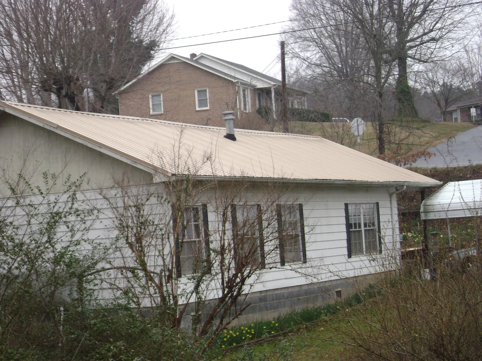 Tan metal roof on a white sided house set into a hillside — Commercial Roofing by Roofing Brothers in Sanderson